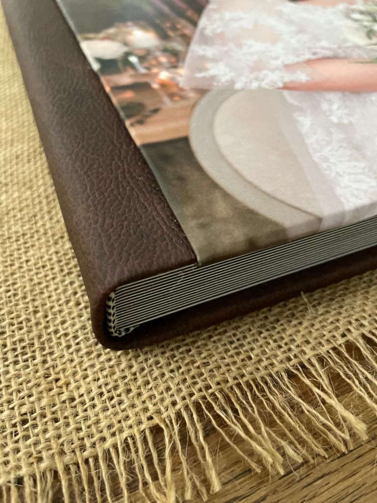 Close-up detail of a brown leather photo album spine and corner resting on textured burlap material.