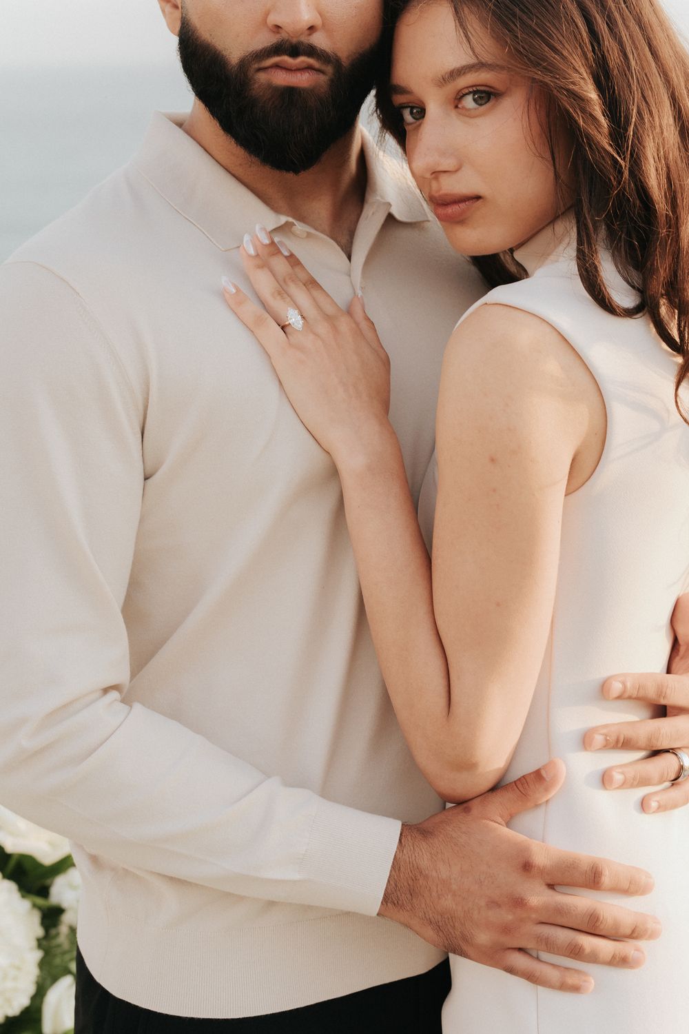 A romantic engagement photo showing a couple in white embracing, with the woman displaying her ring.