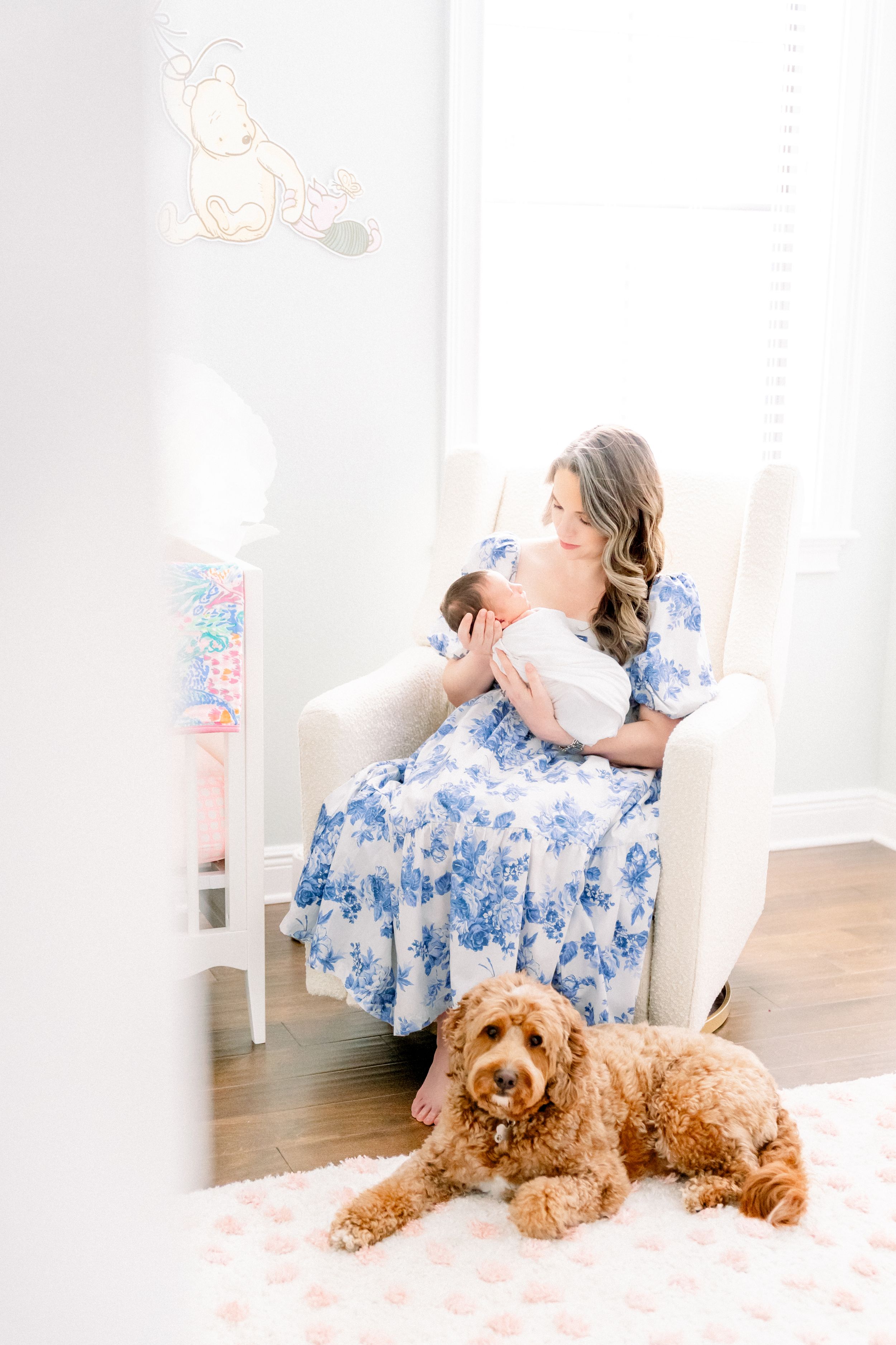 mother in the nursery holding her baby girl in a rocking chair during her newborn session in Tampa while the dog is at her feet