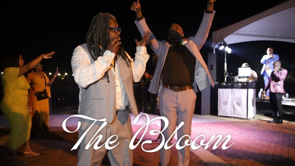 Two performers sing on stage at The Bloom event, with guests and DJ visible in the background at an outdoor night venue.
