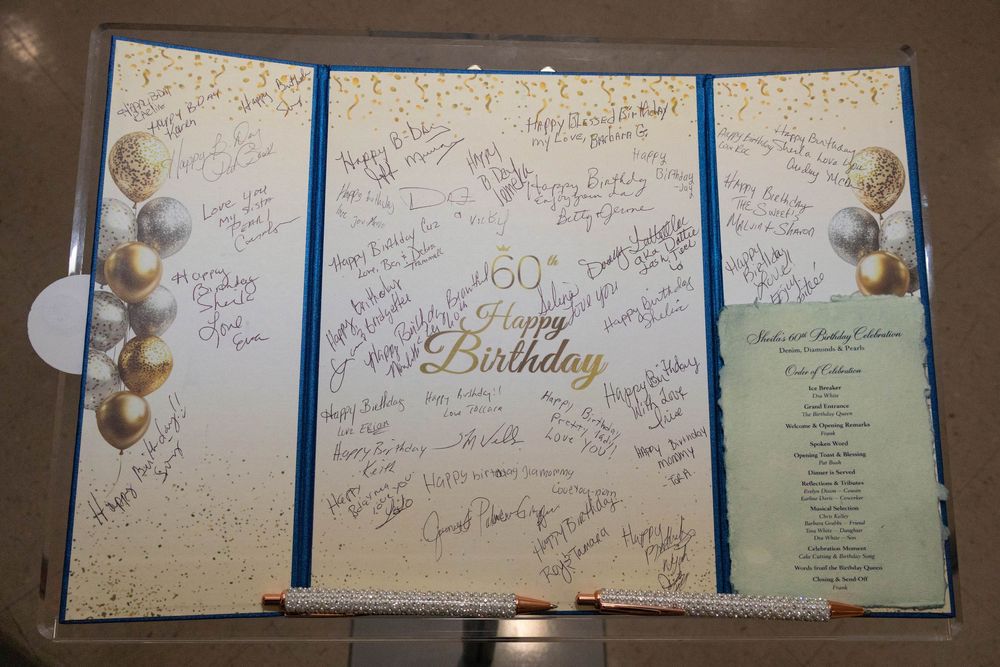 A decorative 60th Happy Birthday signing board with gold balloons and guest signatures displayed on an easel.