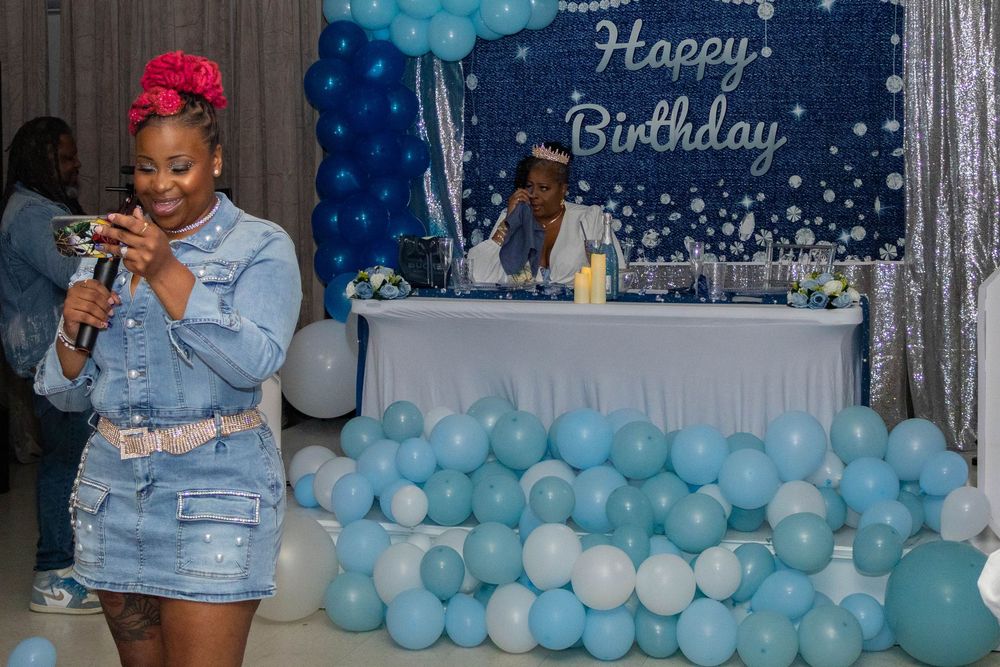 Woman in denim outfit at a blue and white Happy Birthday party with balloon decorations.