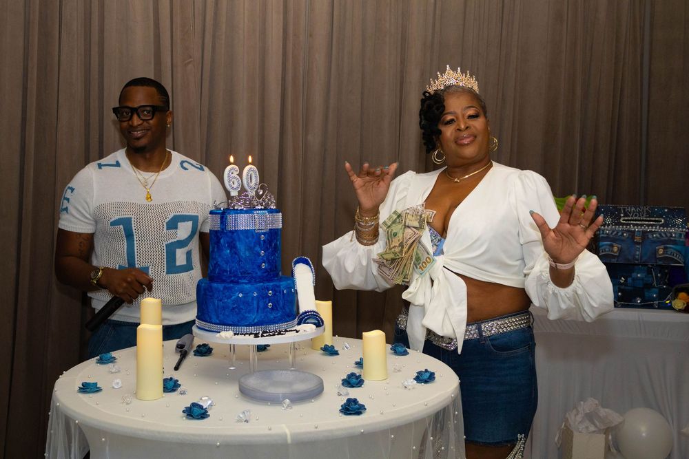Two people celebrate a birthday with a blue tiered cake, candles, and decorations at an elegant party.