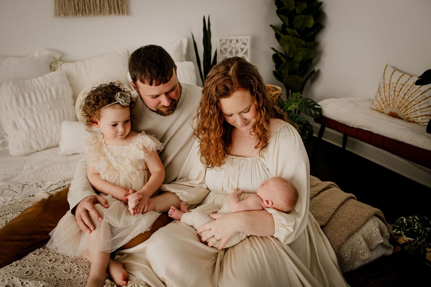 Curly red-headed mother of two holding her new baby in a boho studio photography session