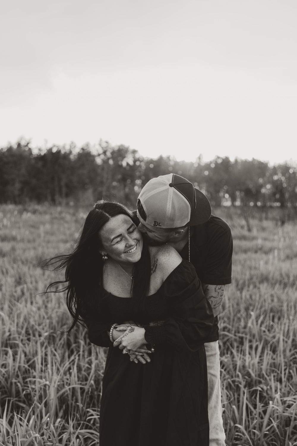 A romantic black and white photo series of a couple embracing in a grassy field at sunset.