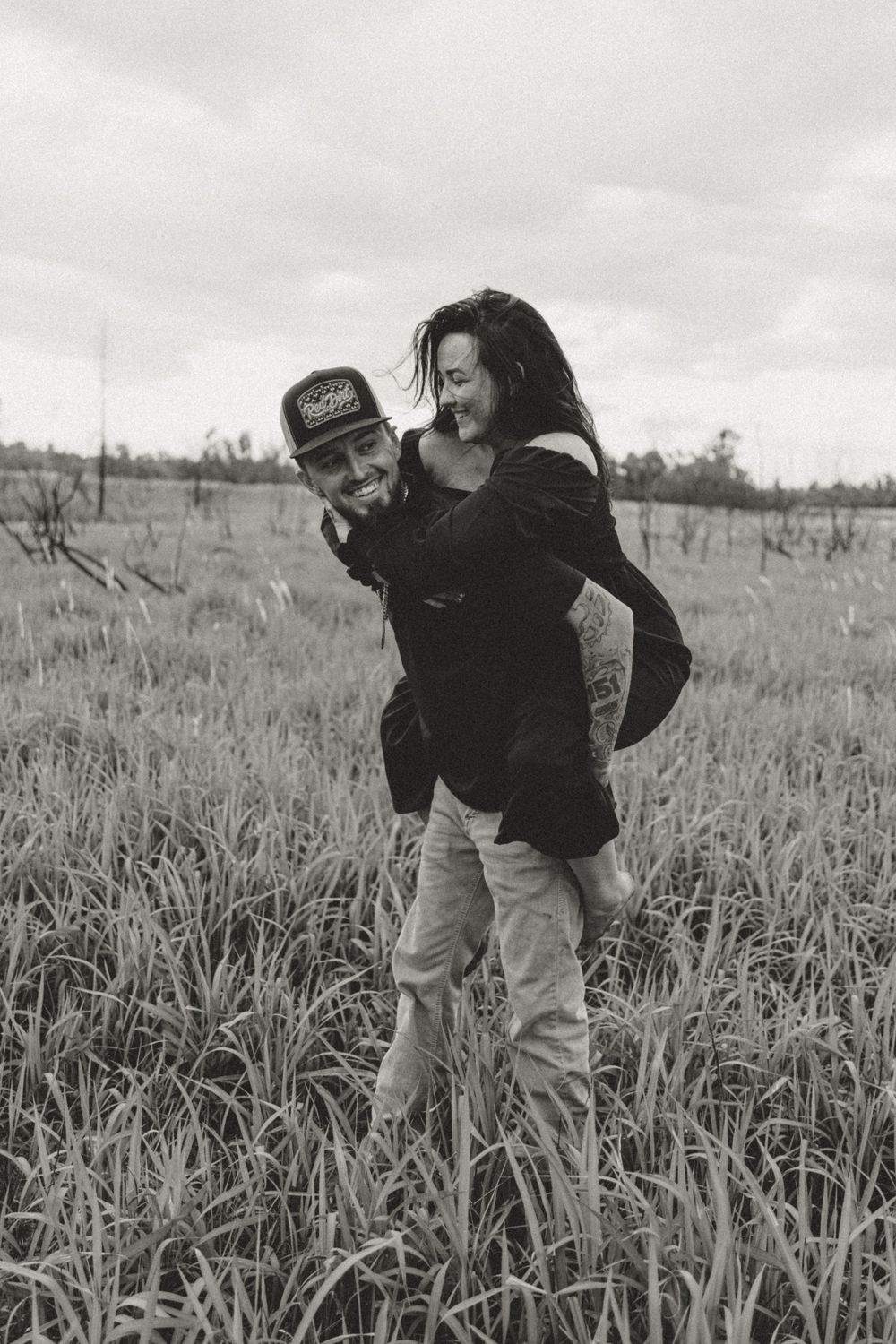 A playful couple sharing a romantic moment in a grass field on an overcast day.