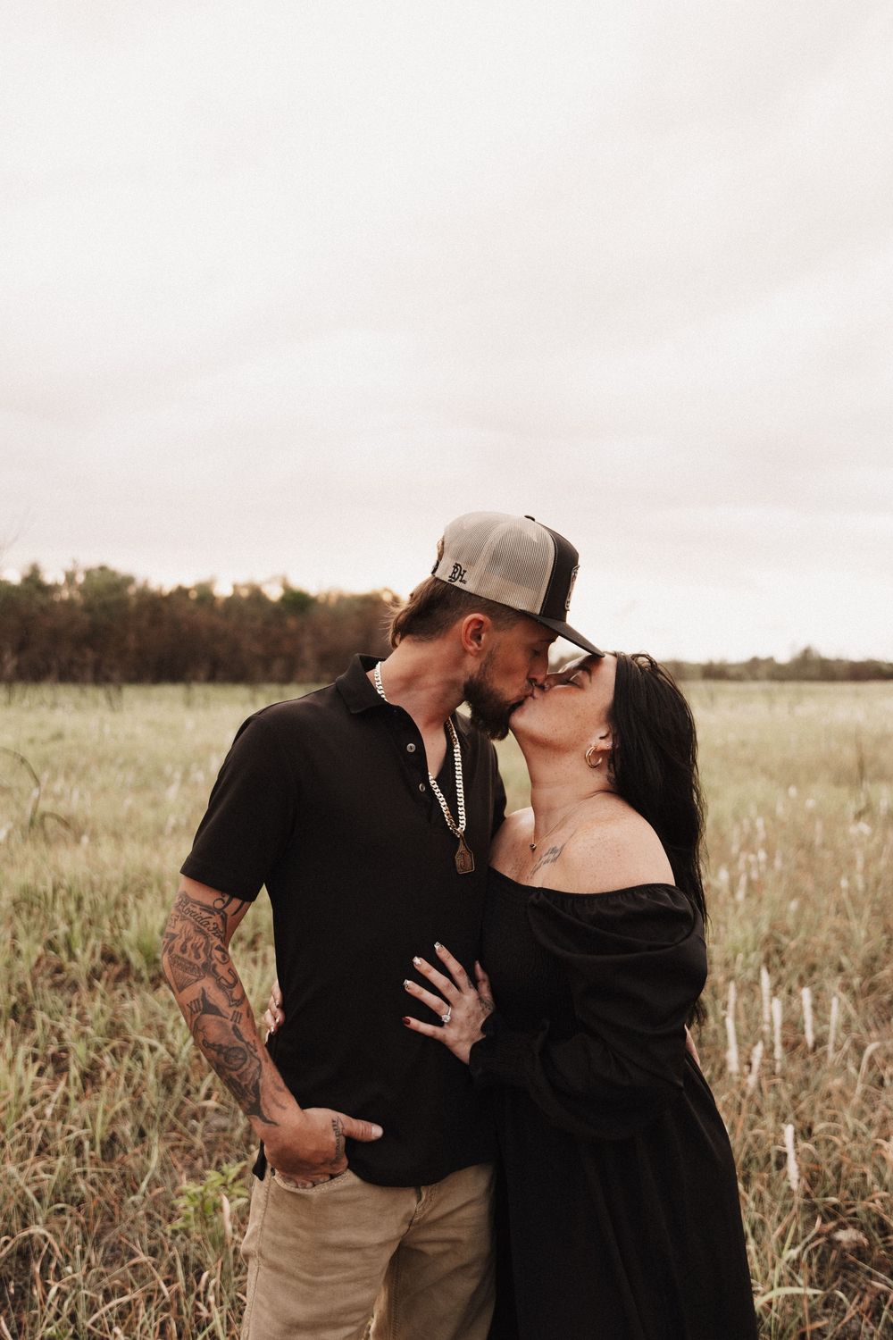 An intimate black and white portrait of a couple embracing in a rustic field setting.
