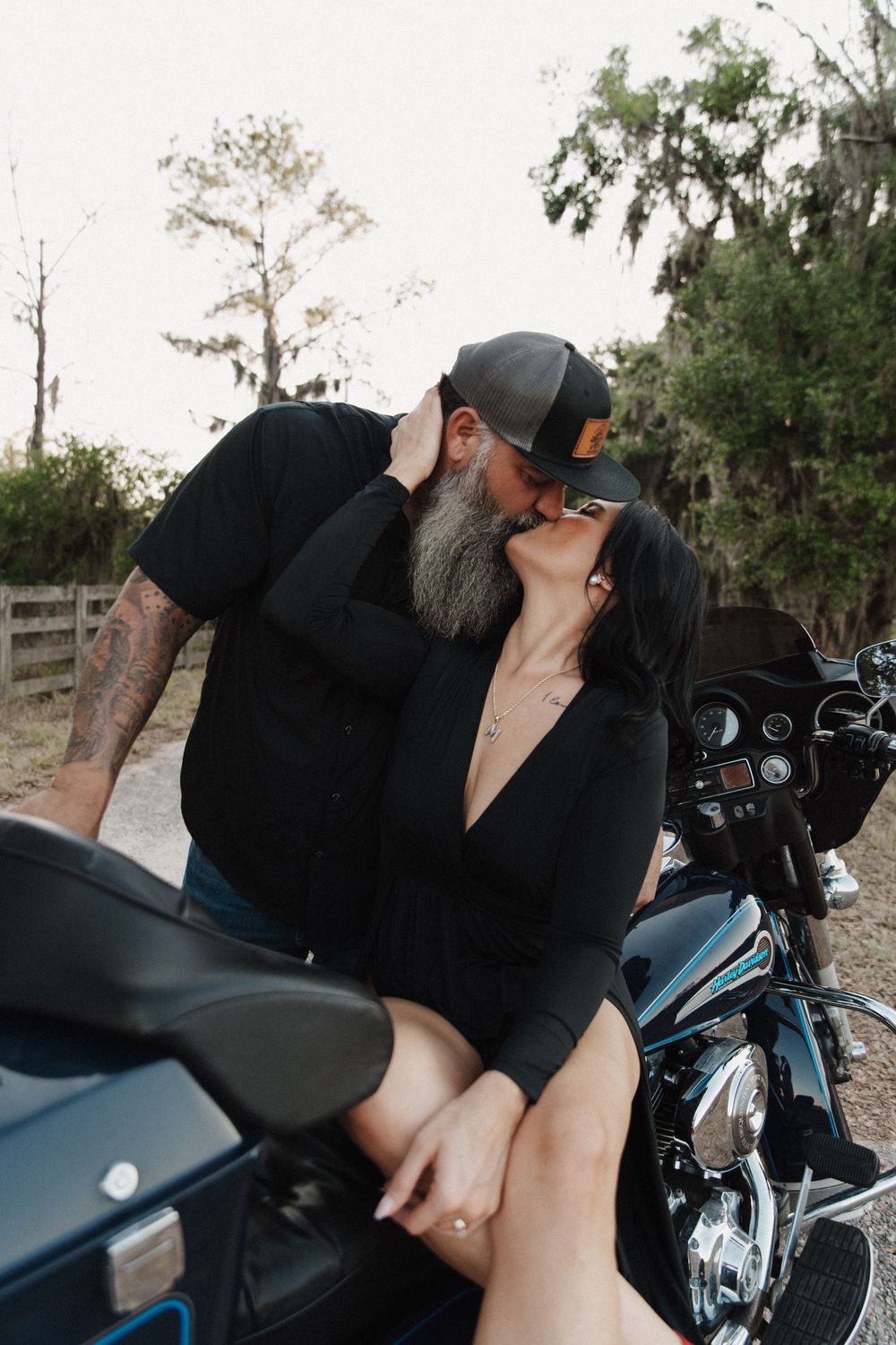 A couple shares a romantic moment on a motorcycle, with Spanish moss-draped trees in the background.