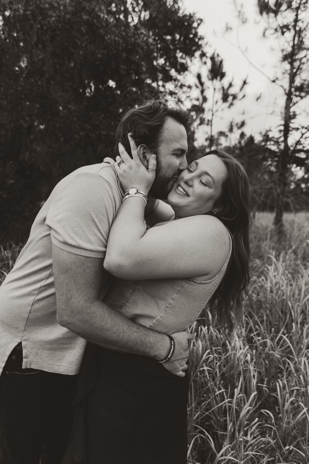 A romantic black and white photo sequence showing an intimate embrace and kiss in a natural outdoor setting with tall grass.