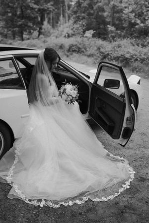 Bruid in zwart-wit bij trouwauto - Elles Yanna Photography