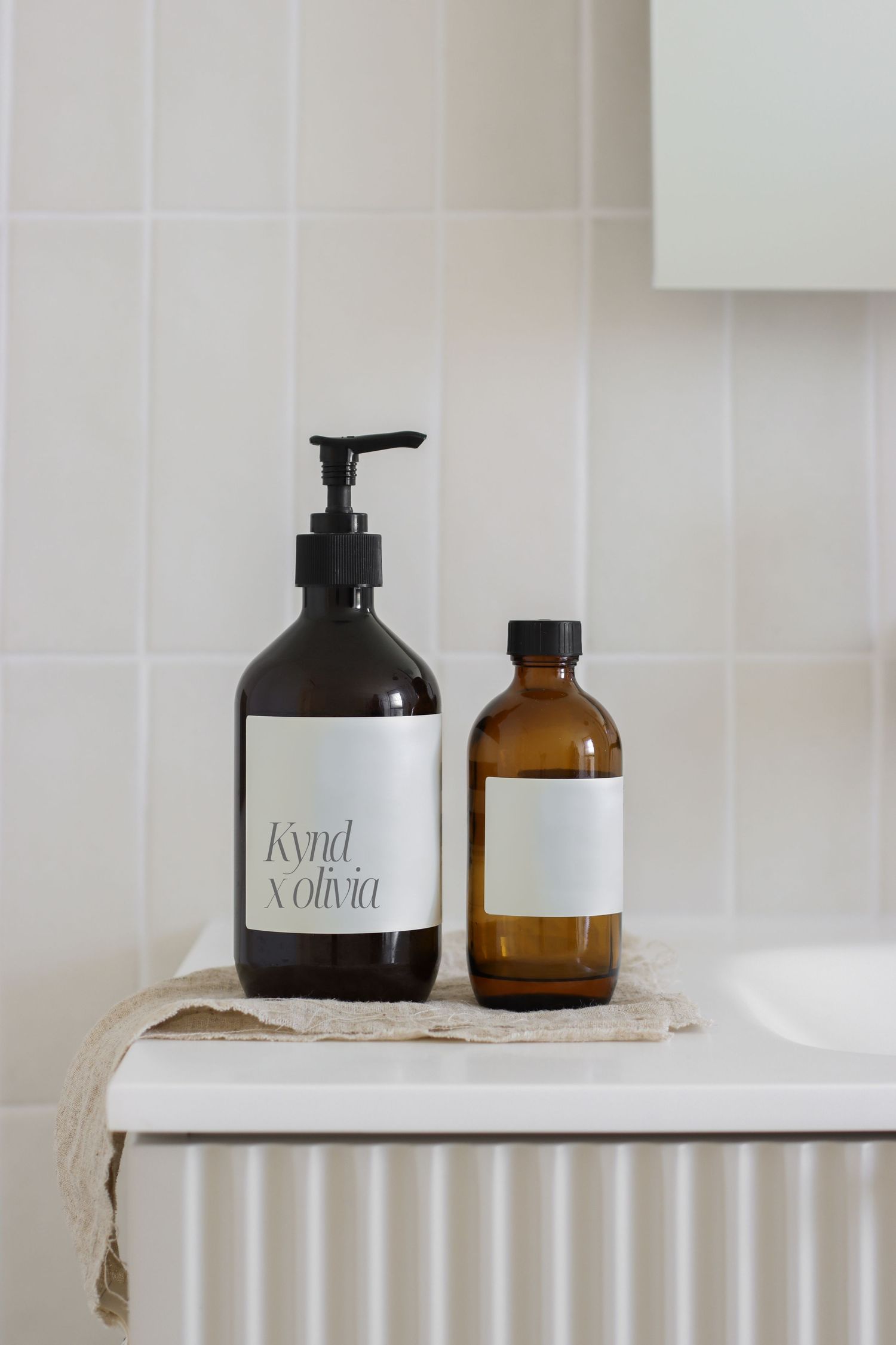 Minimalist bathroom counter with amber glass bottles and white labeled dispensers.