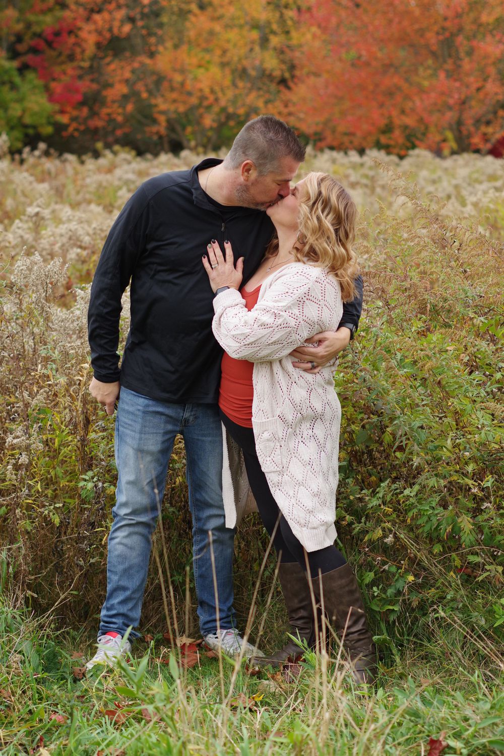 A romantic fall photo shoot in a field with vibrant autumn foliage in the background.