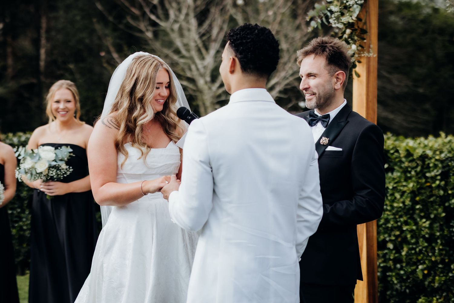 Group wears elegant attire at wedding celebration against rustic stone wall backdrop with white florals and decor.