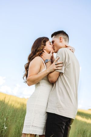 Couple sharing romantic kiss in summer field against blue sky in Branford, CT.