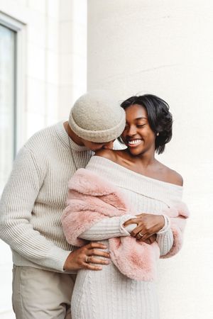 Happy couple in white winter outfits sharing a tender moment by a window in Waterbury, CT.