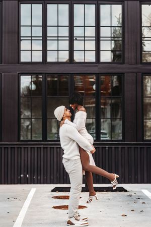 A couple in white outfits dances together in a parking lot with modern buildings in the background in Waterbury, CT.