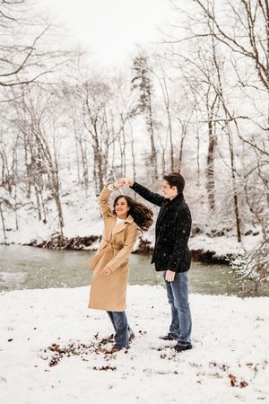 Couple dancing and twirling in the snow surrounded by bare winter trees in Bridgeport, CT.