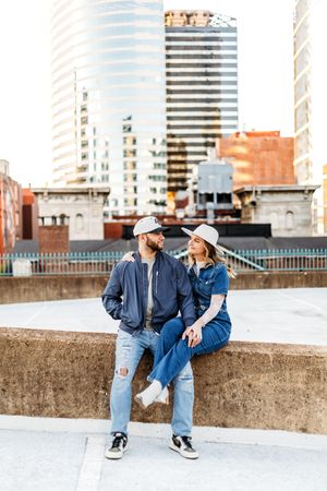 A couple in denim sits together on a concrete wall with New Haven, CT buildings in the background.