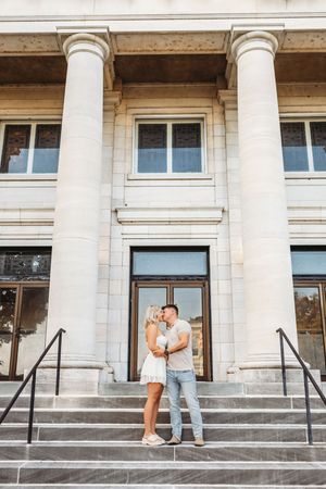 A couple shares a romantic moment on the steps of a grand building with white columns and classical architecture in Hartford, CT.