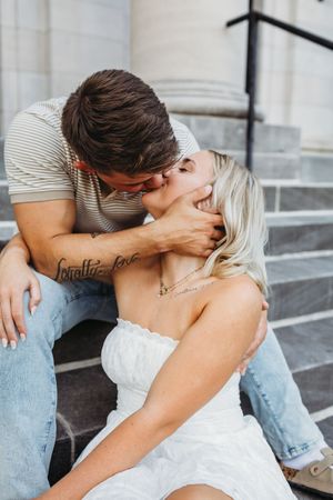 Romantic couple in casual attire sharing intimate kisses while sitting together outdoors in Hartford, CT.