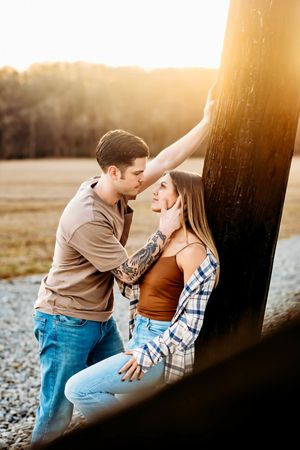 Couple sharing tender moment against golden sunset by rustic post in Bridgeport, CT.