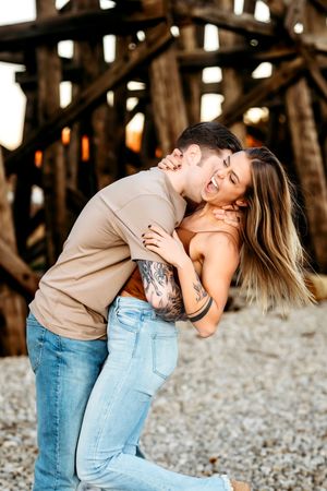Romantic couple embracing near rustic wooden beams during a sunset photoshoot in Bridgeport, CT.