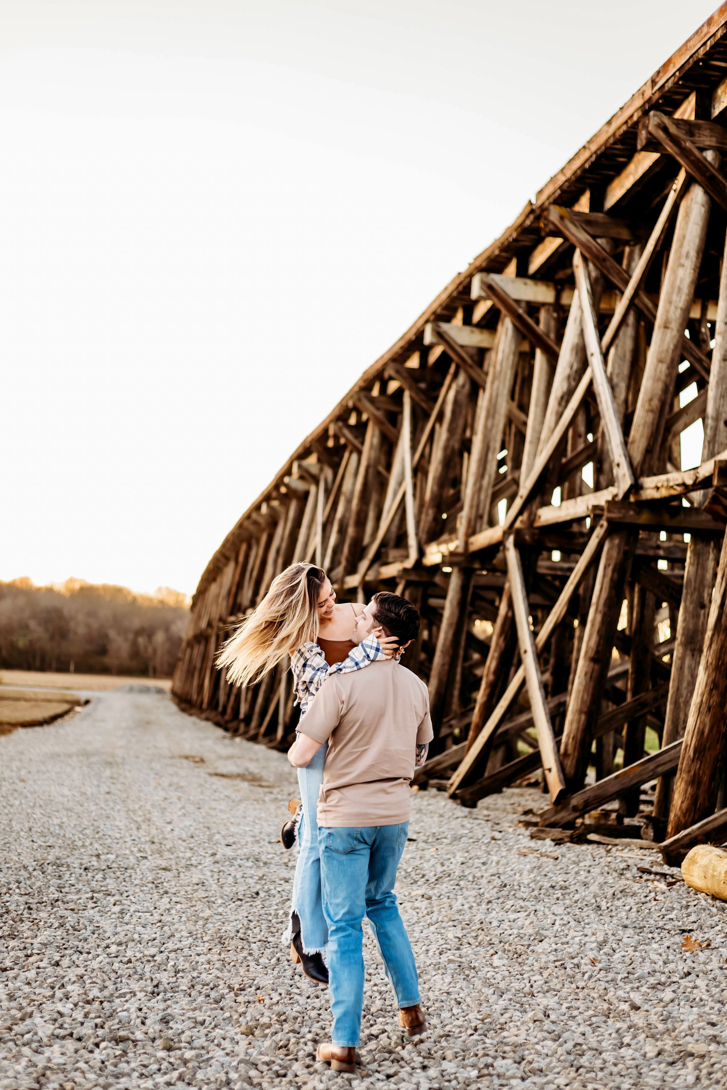 Couple walking and laughing together along a gravel path by an old wooden bridge structure in Bridgeport, CT.