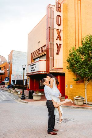 A romantic couple shares an intimate kiss outside a vintage brick theater building in Bridgeport, CT with art deco architectural details.