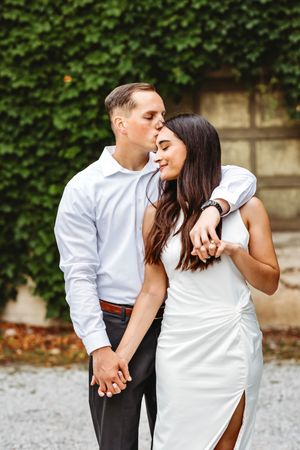 A romantic couple in white and dark attire share tender kisses while posing together in a garden setting in Bridgeport, CT.