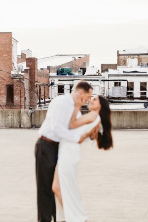 A couple dances together on an urban rooftop in Bridgeport, CT with brick buildings in the background during a romantic moment.