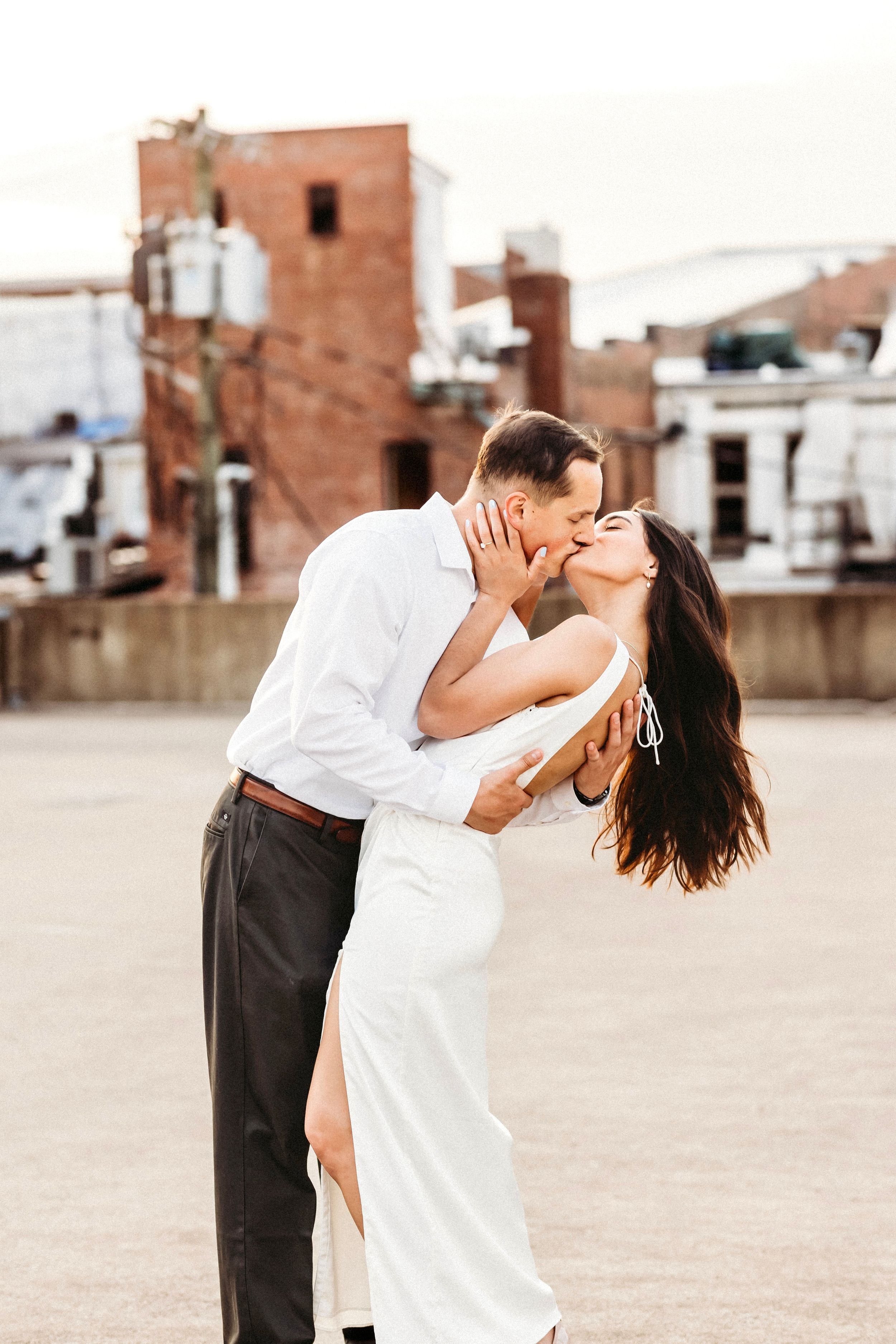 A romantic couple in white and black attire share a passionate kiss on an urban rooftop terrace in Bridgeport, CT.