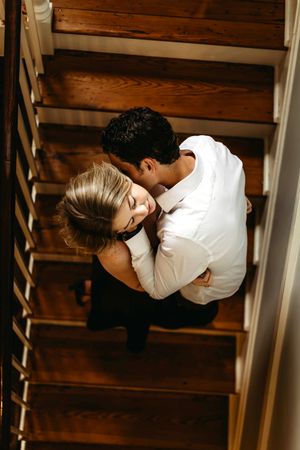 Romantic couple sharing an intimate moment on wooden stairs in a warm interior setting in Branford, CT.