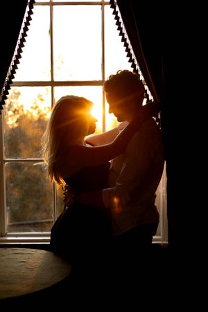 Silhouetted couple embracing by window during golden sunset in Branford, CT.