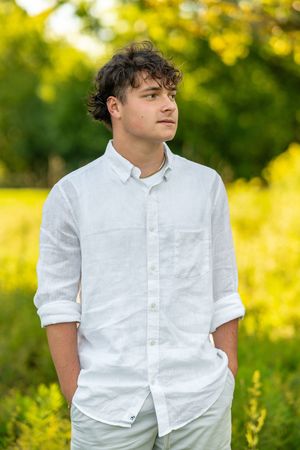 Young person in white button-down shirt poses outdoors against blurred yellow and green natural background.