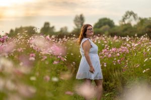 Woman in white dress standing among pink wildflowers at sunset.