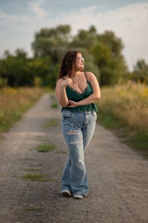 Woman in casual attire poses on rural dirt path during golden hour.