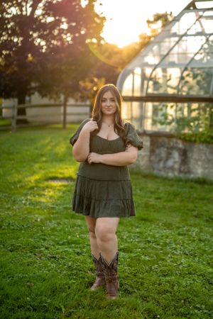 A green dress and cowboy boots ensemble photographed at sunset near a greenhouse in a garden setting.