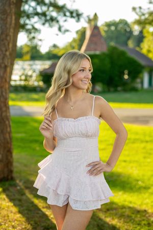 A woman in a white eyelet summer dress twirls playfully in a sunlit grassy field during golden hour.