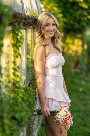 Portrait in a garden setting with someone wearing a light pink dress and holding a small bouquet of flowers.