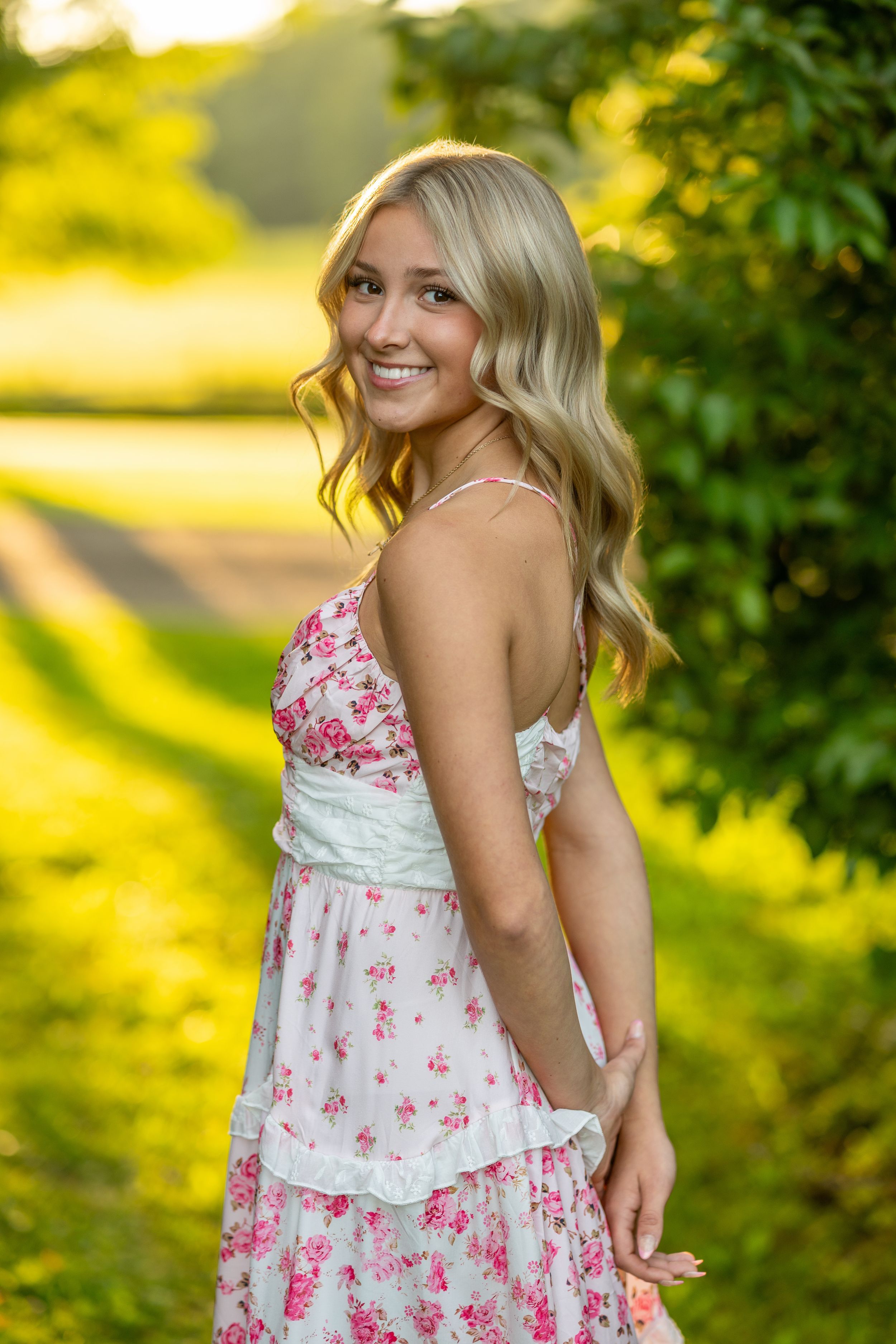 A person in a white and pink floral sundress poses outdoors against a bright yellow and green background.
