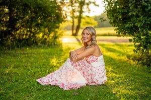 Sunset portrait in a grassy field with someone wearing a floral dress sitting on the ground.