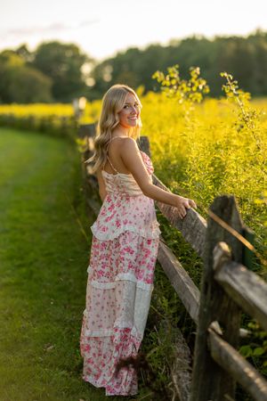 Golden hour portrait by a fence with someone in a pink and white floral maxi dress.