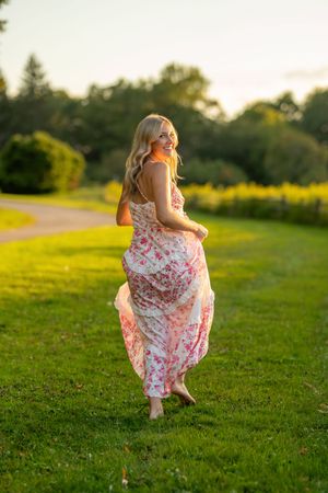 A woman in a flowing floral dress twirls on a grassy hill during golden hour sunset.