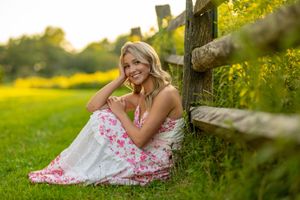 A person in a floral dress poses gracefully in a sunlit meadow near a tree during golden hour.