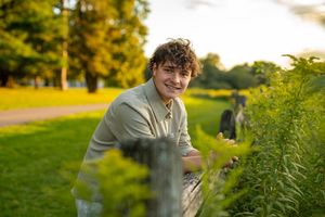 A person wearing a gray t-shirt poses casually among tall greenery in a backyard garden setting.
