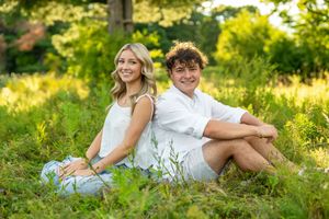 Two people sitting back-to-back in a sunny meadow with tall grass and wildflowers on a summer afternoon.