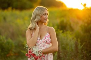 Woman in floral dress poses in golden sunlit field during sunset photoshoot.
