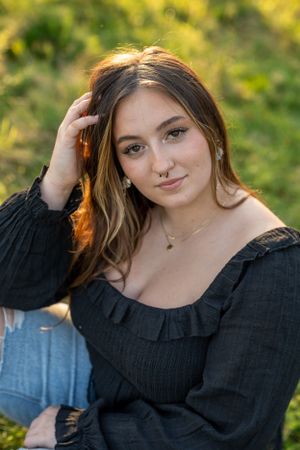 Portrait of woman in black ruffle top against sunlit natural background.