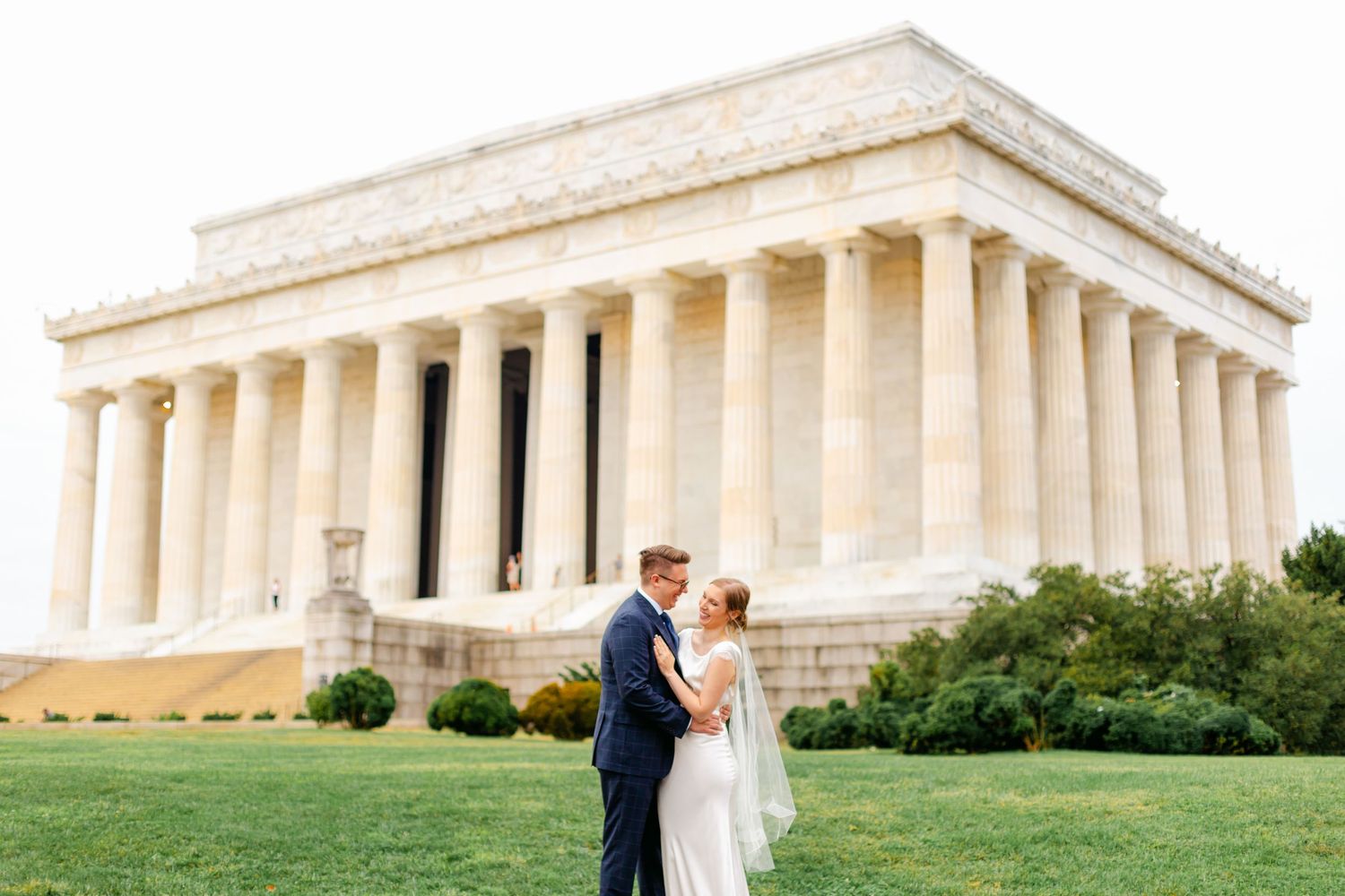 Bride and groom embrace on the lawn in front of the Lincoln Memorial in Washington DC.