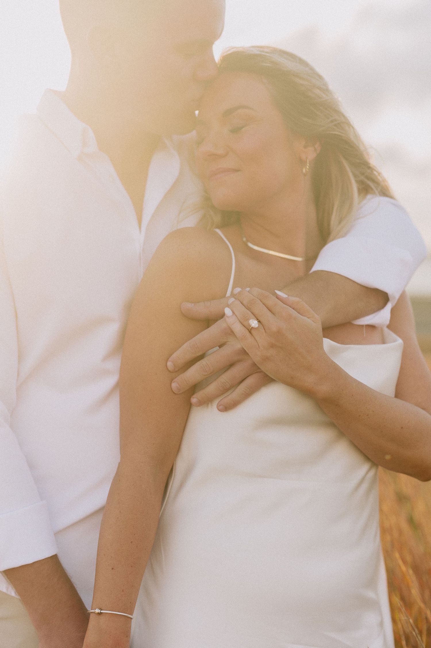 Dreamy sunlit close-up shots of couple embracing in white attire.